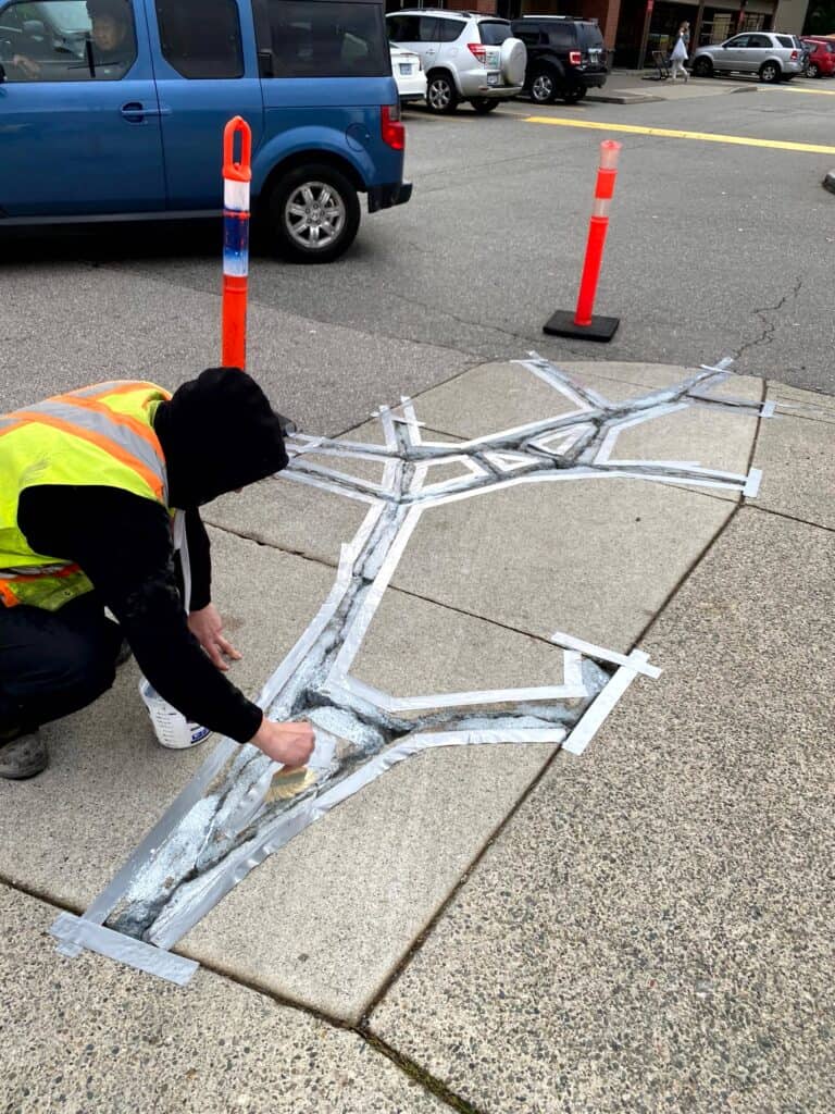 A person in a black hoodie and yellow safety vest is repairing a concrete sidewalk.