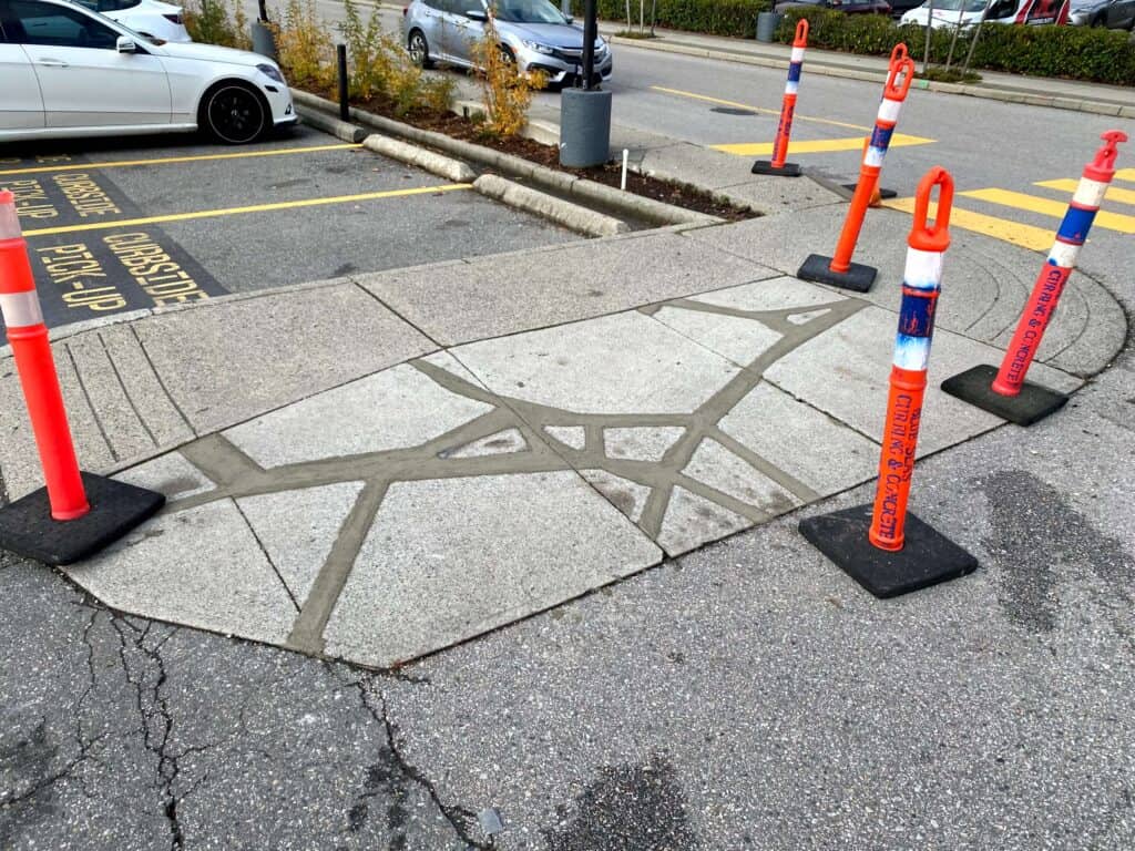 A freshly repaired section of concrete pavement is surrounded by four orange traffic cones.