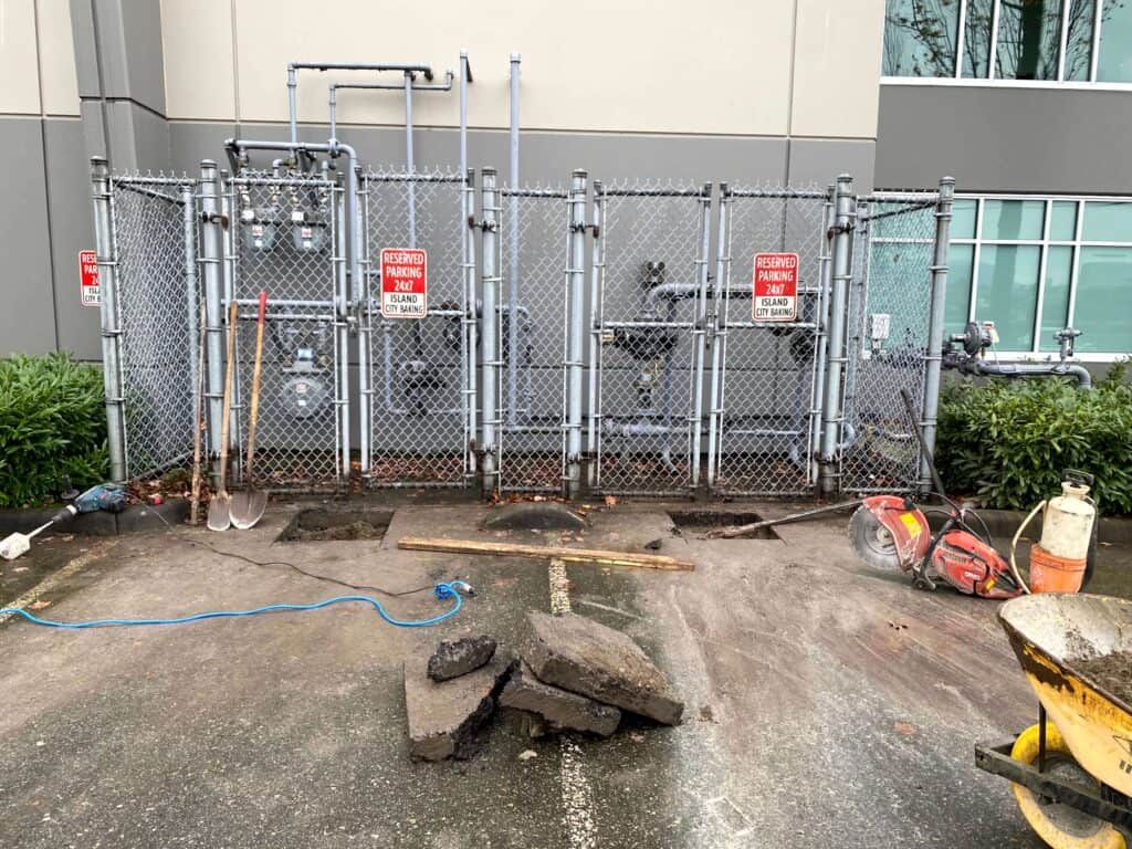 The ground is partially dug up, with concrete chunks, asphalt pieces, and a wheelbarrow nearby.