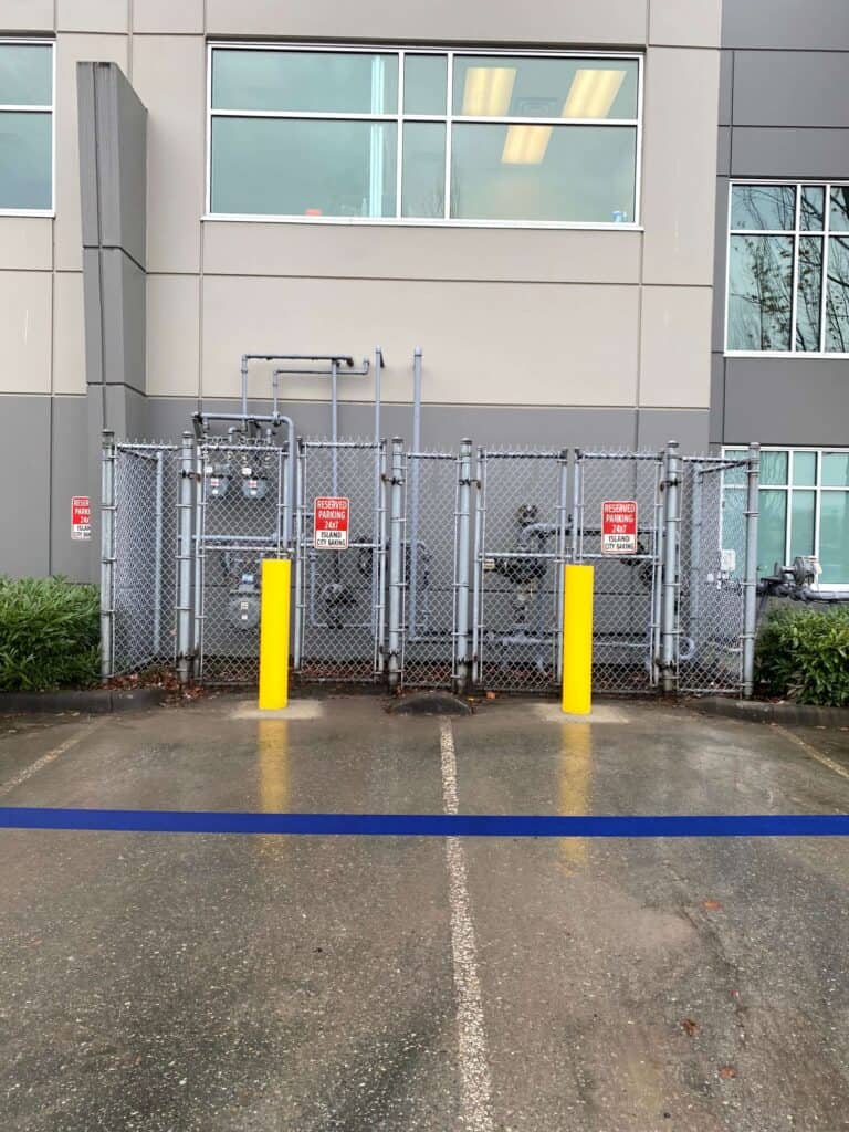 Two bright yellow bollards stand firmly on the concrete, in front of the fence.