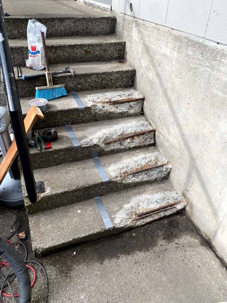 A set of outdoor concrete steps shows visible wear and erosion. Nearby lie repair tools.
